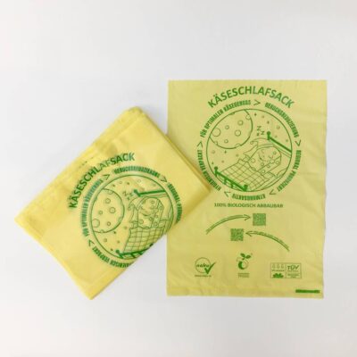 Das Frontdesign des Naku Käseschlafsacks, einem Käsebeutel aus Maisstärke, im 100er Pack für die Käsetheke im Einzelbild und als zusammengeschlagenes Pack.